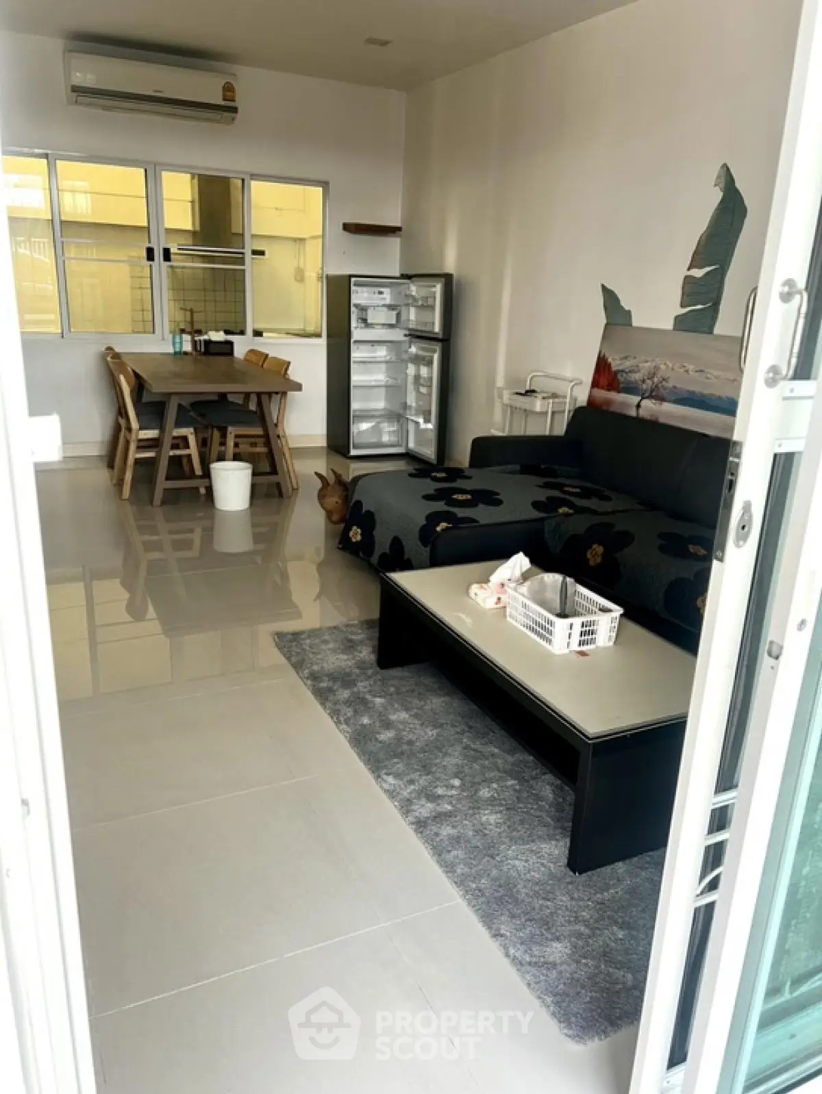 Modern living room with sleek furniture and dining area, featuring large windows and air conditioning.
