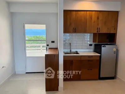 Modern kitchen with wooden cabinets and compact fridge, featuring a scenic balcony view.