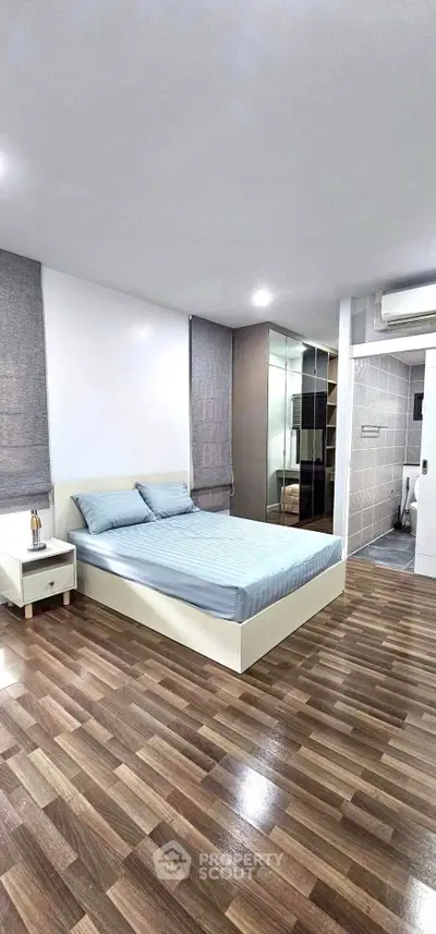 Modern bedroom with sleek design and wooden flooring, featuring a comfortable bed and mirrored wardrobe.