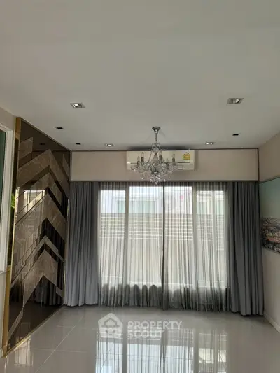 Elegant living room with chandelier and large windows, featuring modern design and luxurious finishes.