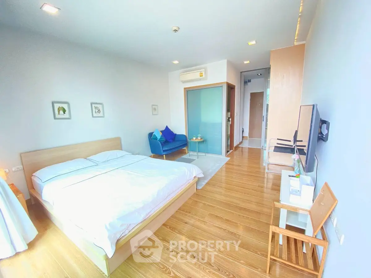 Spacious modern bedroom with wooden flooring and cozy seating area