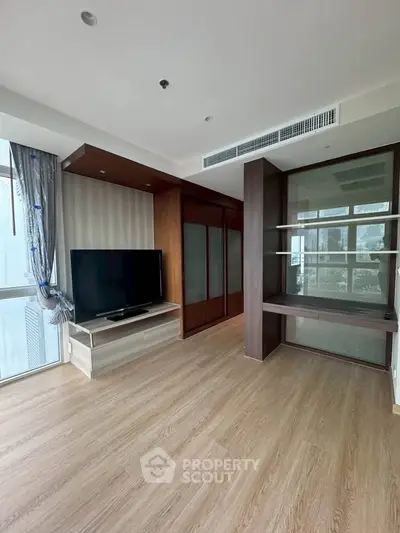 Spacious living room with modern design and large TV, featuring wooden flooring and ample natural light.