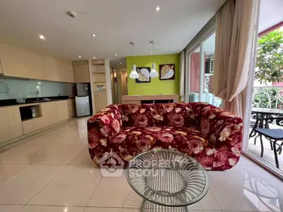 Spacious living room with floral sofa and open kitchen layout, featuring modern decor and balcony access.