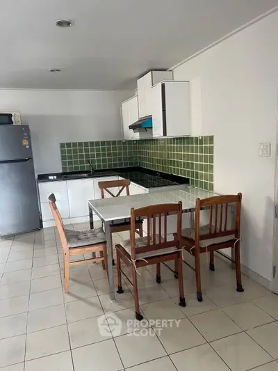 Modern kitchen with green tile backsplash and dining area in a cozy apartment.