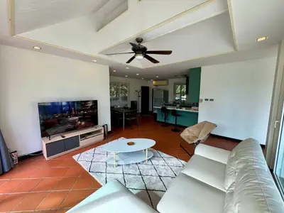 Spacious living room with modern decor and open kitchen layout, featuring a ceiling fan and large TV.