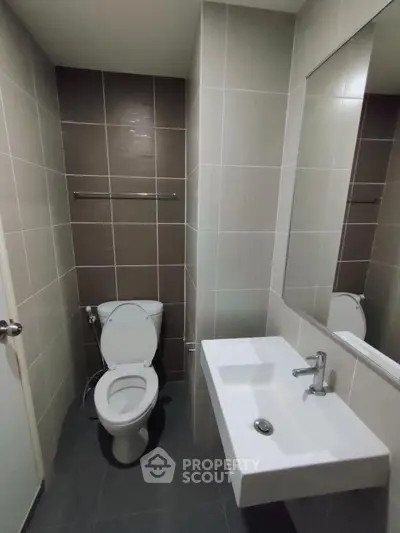 Modern bathroom with sleek design and neutral tiles, featuring a toilet and a wall-mounted sink.