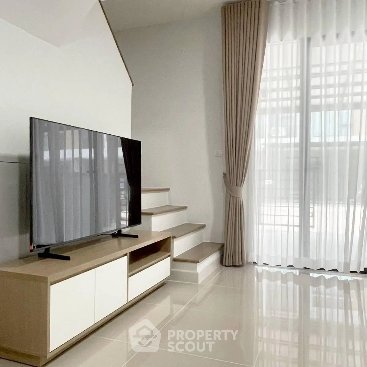 Modern living room with sleek TV setup and elegant staircase design.