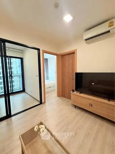 Modern living room with TV, air conditioning, and view into bedroom and balcony.