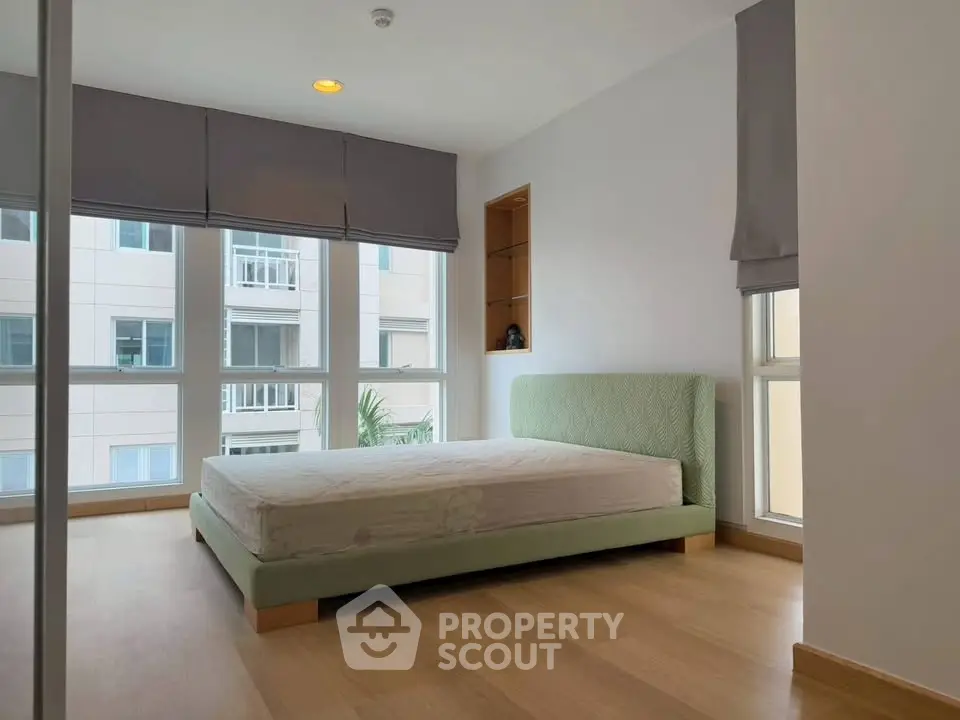 Spacious bedroom with large windows and modern design in a high-rise apartment.