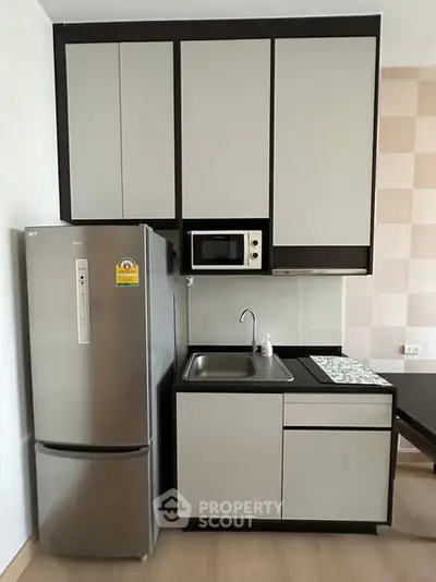 Modern kitchen with sleek cabinets and stainless steel fridge in compact layout.
