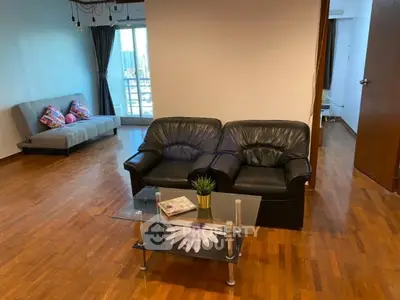 Spacious living room with wooden flooring, modern furniture, and large windows offering natural light.