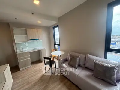 Modern living room with kitchenette and city view, featuring sleek furniture and large windows.