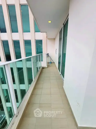 Spacious balcony with glass railing and modern building view, perfect for relaxation.