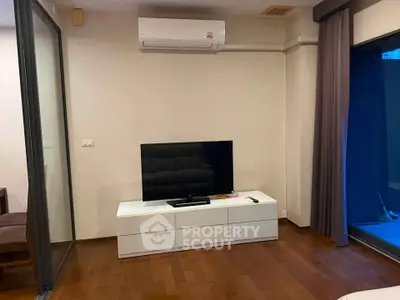 Modern living room with sleek TV setup and air conditioning, featuring elegant wooden flooring and glass partition.