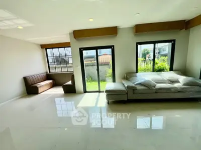 Spacious living room with large windows and garden view, featuring modern furniture and abundant natural light.
