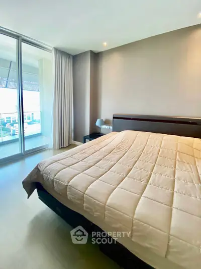 Spacious bedroom with large windows and balcony access in modern apartment.