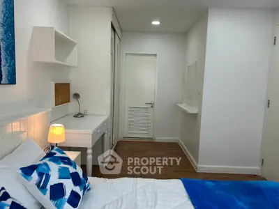 Cozy bedroom with modern decor and wooden flooring, featuring a desk and stylish blue accents.