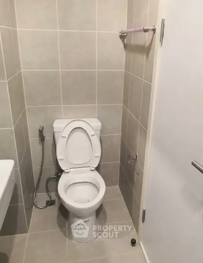 Modern bathroom with tiled walls and floor, featuring a toilet and bidet spray.