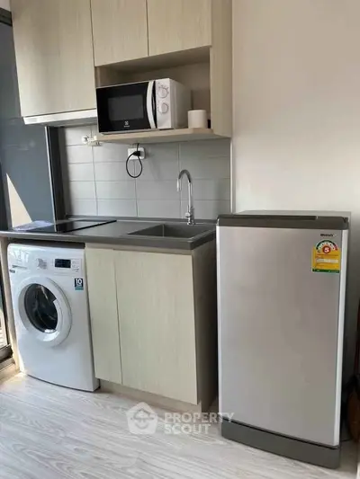Modern kitchen with washing machine, microwave, and fridge in compact layout.
