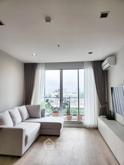 Modern living room with large window and city view, featuring a cozy sofa and sleek TV setup.