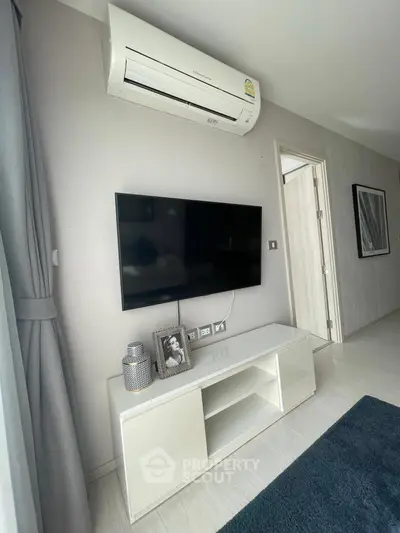 Modern living room with wall-mounted TV and air conditioning unit, featuring sleek white furniture and stylish decor.