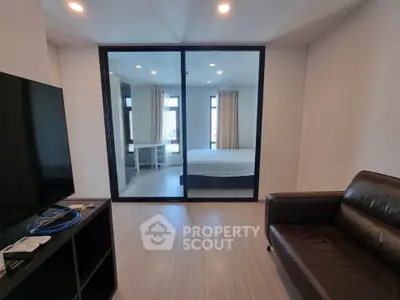 Modern living room with sleek design and glass partition leading to a cozy bedroom.