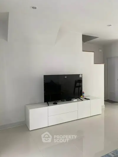 Modern living room with sleek white TV stand and flat-screen TV, showcasing minimalist design.