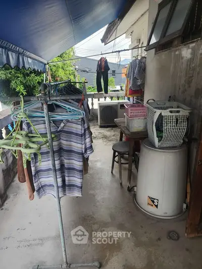 Outdoor laundry area with washing machine and clothes drying under a canopy.