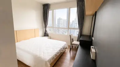 Modern bedroom with large windows offering city views, featuring a cozy bed and stylish furnishings.