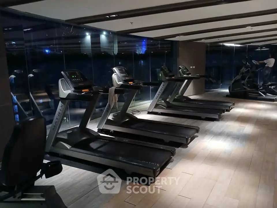 Modern gym with multiple treadmills and wooden flooring in a luxury building.