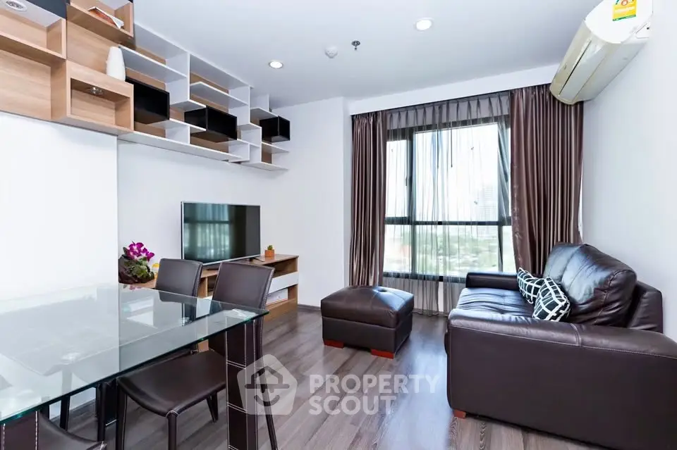 Modern living room with sleek furniture and large window offering city views.