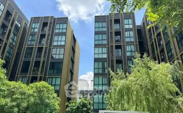 Modern apartment building exterior with lush greenery and clear blue sky.