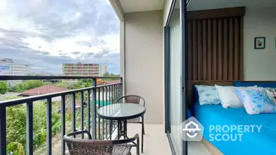 Spacious balcony with outdoor seating connected to a cozy bedroom with vibrant blue bedding, offering a serene urban view and ample natural light.