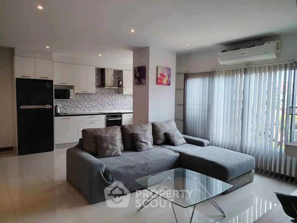 Modern open-plan living room with sleek kitchen, stylish sofa, and large windows for natural light.