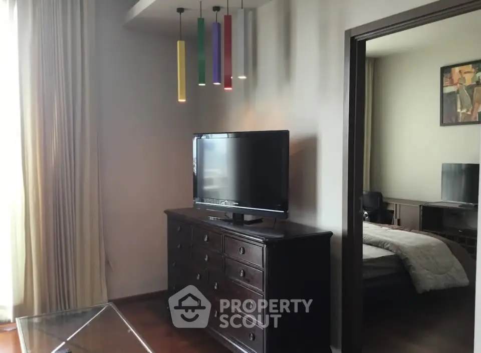 Modern living room with stylish lighting and TV, leading to a cozy bedroom.
