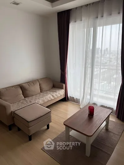 Cozy living room with a beige sofa, wooden coffee table, and city view through large window.