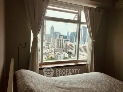 Cozy bedroom with stunning city view from large window, perfect urban retreat.