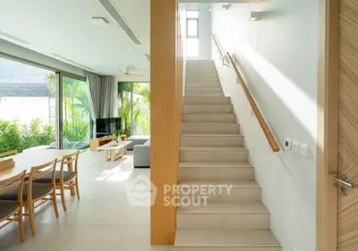 Spacious modern living room with large windows and staircase, featuring elegant dining area and lush garden view.