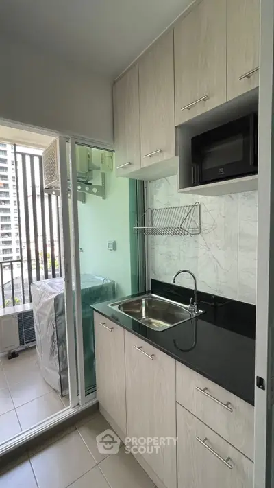 Modern kitchen with sleek cabinetry and balcony view, featuring a compact layout and stylish finishes.