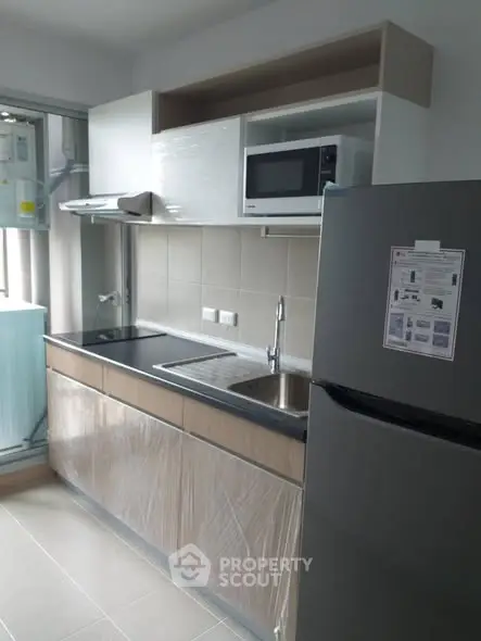 Modern kitchen with sleek cabinetry, microwave, and stainless steel fridge in a contemporary apartment.