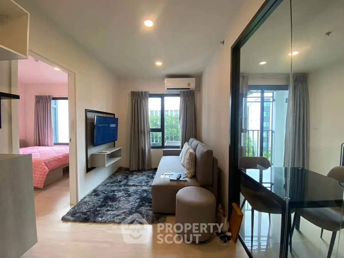 Modern living room with cozy seating and wall-mounted TV, adjacent to a stylish bedroom.