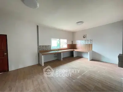 Spacious kitchen with wooden flooring and ample natural light, featuring a minimalist design and large countertops.