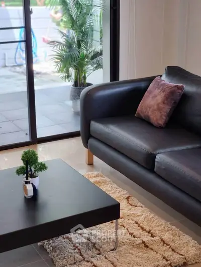 Modern living room with sleek black sofa and stylish decor overlooking a lush garden view.