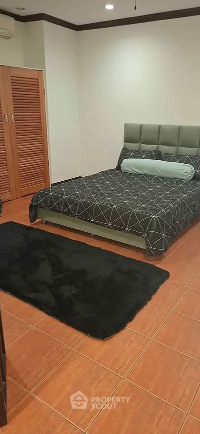 Spacious bedroom with modern decor and wooden flooring, featuring a stylish bed and cozy rug.