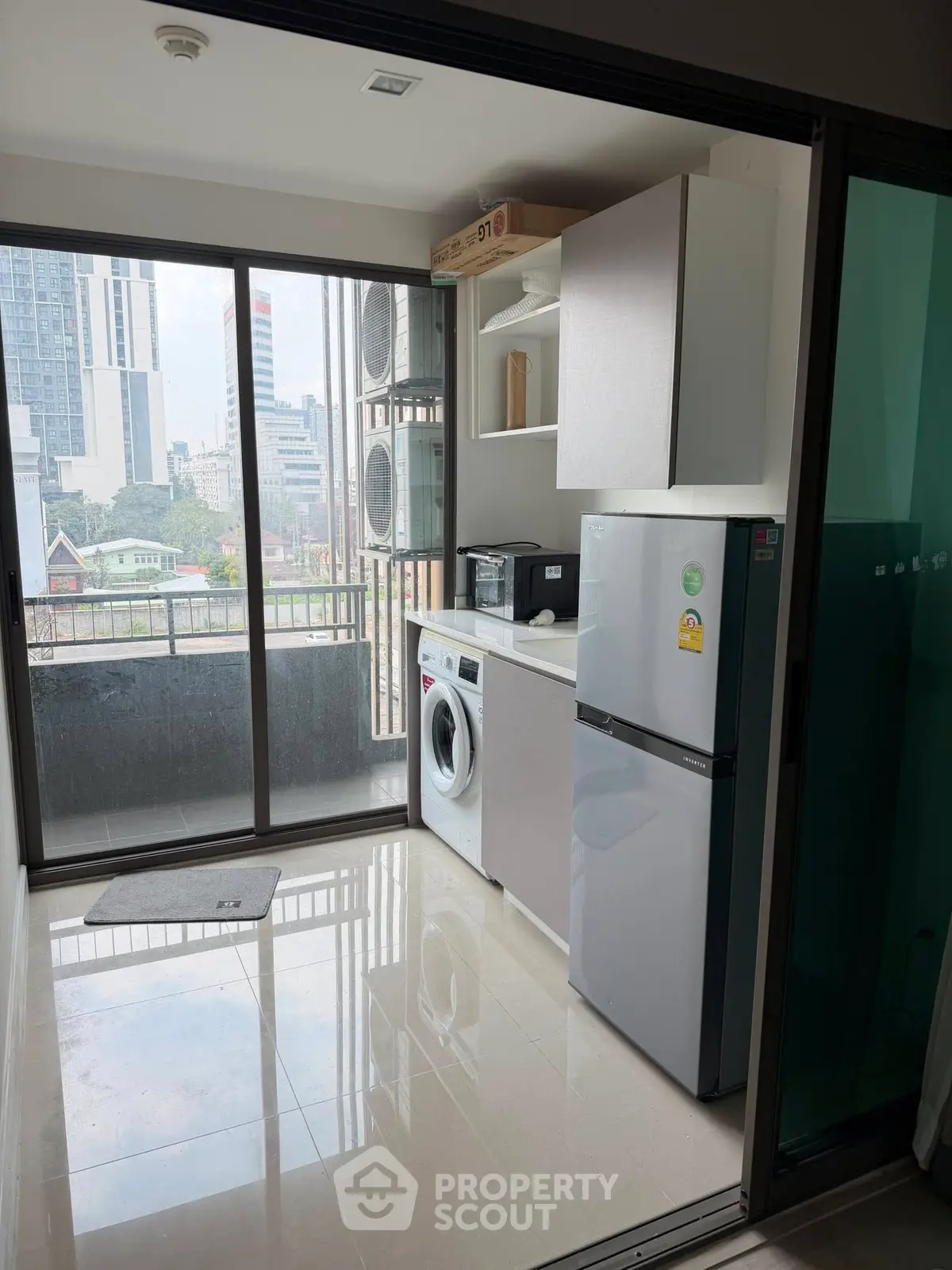 Modern kitchen with balcony view, featuring washing machine and fridge in a sleek apartment setting.