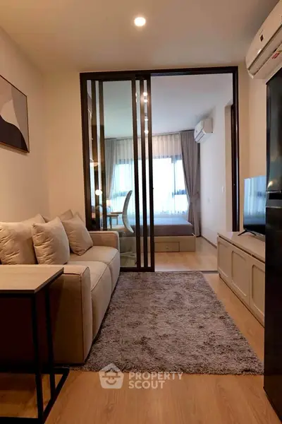 Modern living room with cozy sofa and view into stylish bedroom through glass doors.