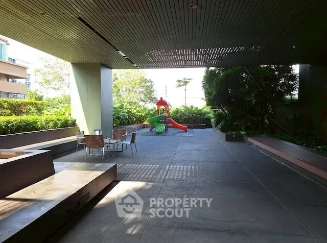 Spacious outdoor common area with seating and children's play area in modern residential complex.