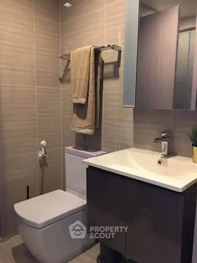 Modern bathroom with sleek fixtures and neutral tones, featuring a compact vanity and towel rack.