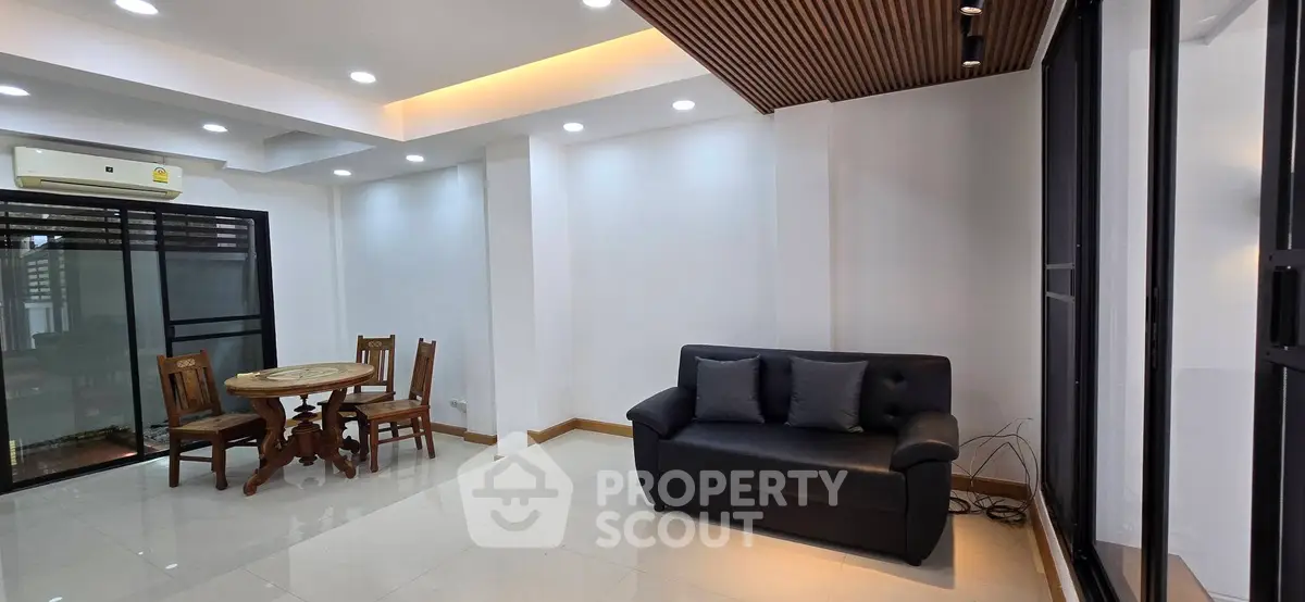 Spacious modern living room with sleek black sofa and elegant dining set, featuring ambient lighting and large windows.