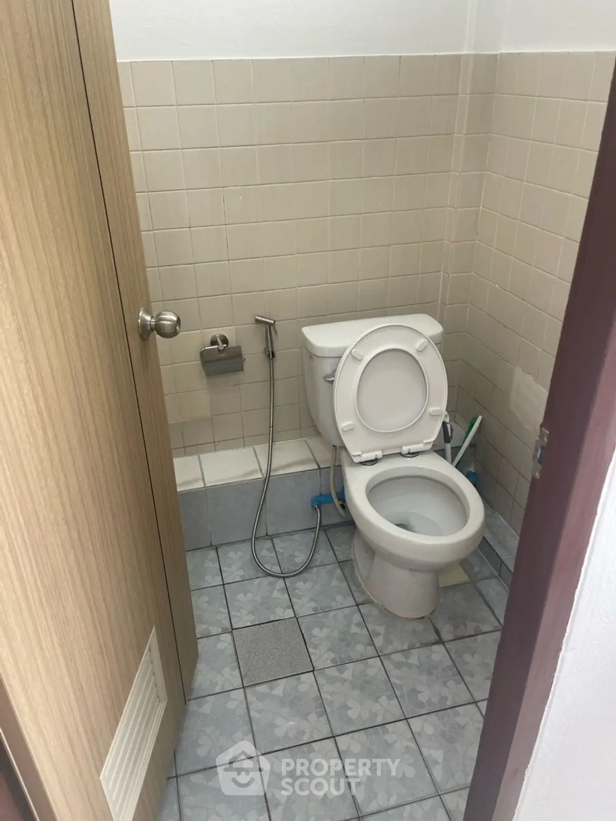 Compact bathroom with tiled walls and floor, featuring a toilet and bidet spray.